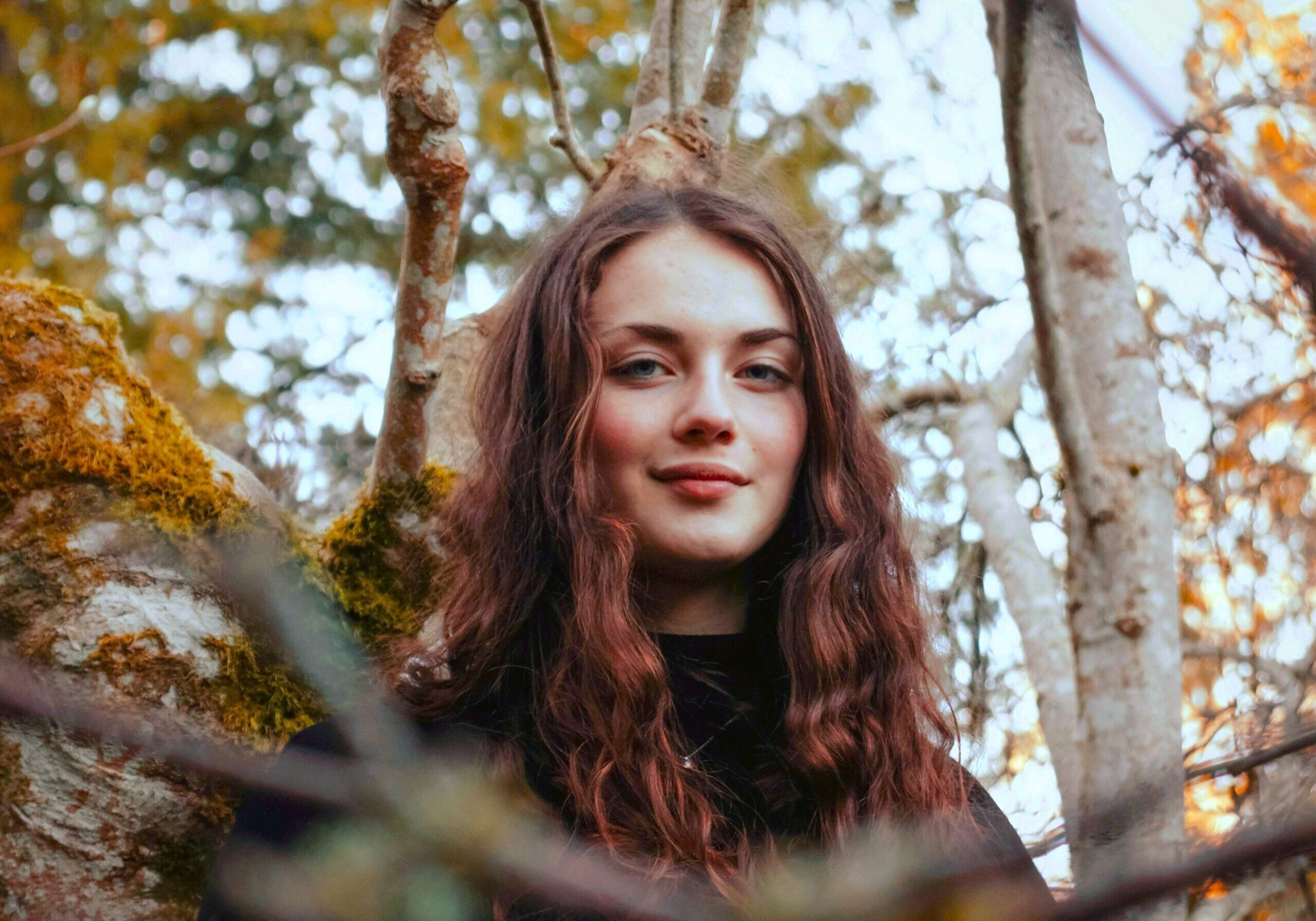 Image of a woman standing near a fall-colored tree.